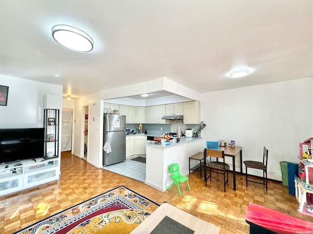 kitchen featuring white cabinets, backsplash, kitchen peninsula, stainless steel fridge, and light parquet flooring