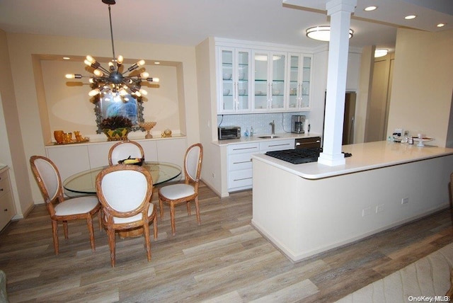 kitchen featuring pendant lighting, white cabinets, sink, light hardwood / wood-style floors, and decorative columns