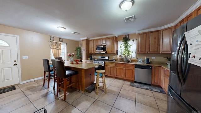 kitchen with a kitchen bar, stainless steel appliances, sink, light tile patterned floors, and a center island