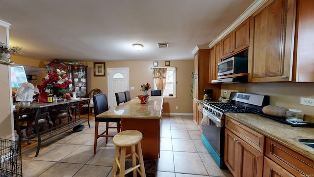 kitchen featuring light stone countertops, stainless steel appliances, light tile patterned floors, a kitchen bar, and a kitchen island