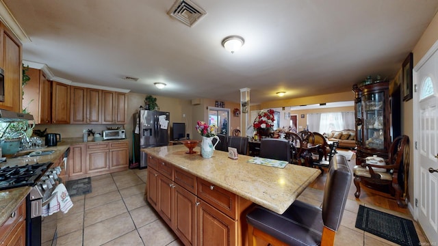 kitchen featuring a center island, light tile patterned floors, light stone countertops, appliances with stainless steel finishes, and a kitchen bar