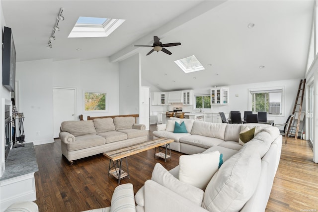 living room featuring dark hardwood / wood-style flooring, a skylight, high vaulted ceiling, and ceiling fan