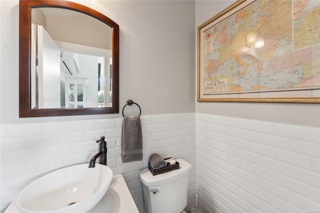 bathroom with toilet, tile walls, and sink