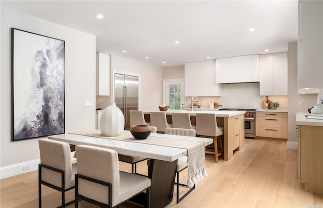 kitchen featuring high end range, a kitchen breakfast bar, light wood-type flooring, a kitchen island with sink, and white cabinets