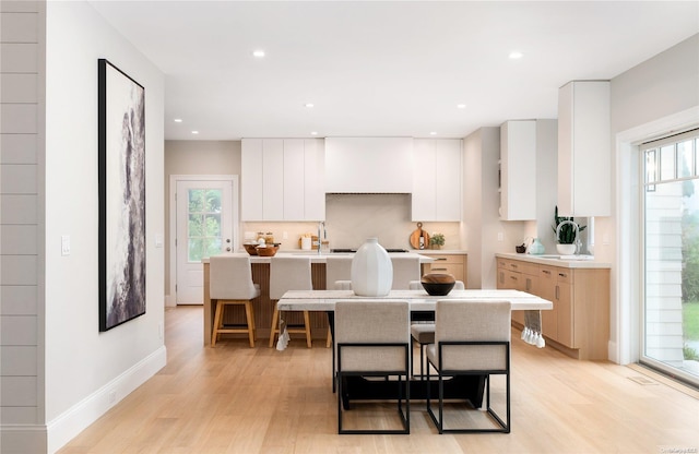 kitchen with a wealth of natural light, white cabinets, light hardwood / wood-style floors, and an island with sink