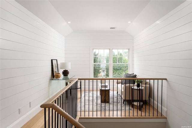 hallway with wooden walls, light hardwood / wood-style flooring, and lofted ceiling