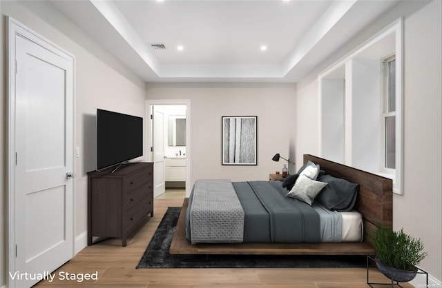 bedroom featuring a raised ceiling, connected bathroom, and light hardwood / wood-style floors