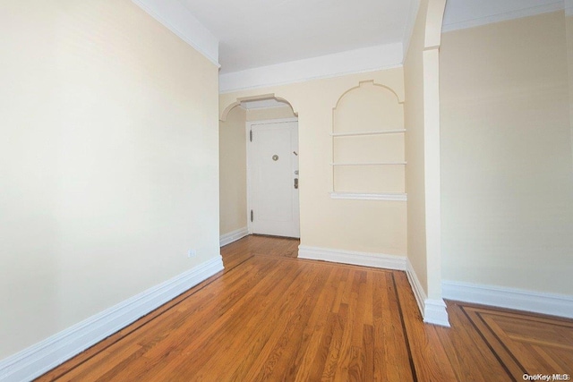 unfurnished room with built in shelves, ornamental molding, and hardwood / wood-style flooring