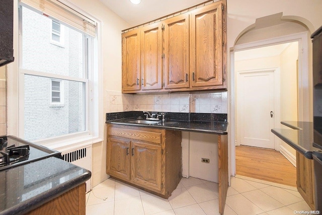 kitchen featuring dark stone countertops, light tile patterned floors, sink, and radiator