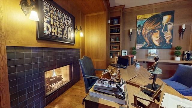 home office with a fireplace, hardwood / wood-style floors, built in shelves, and wood walls