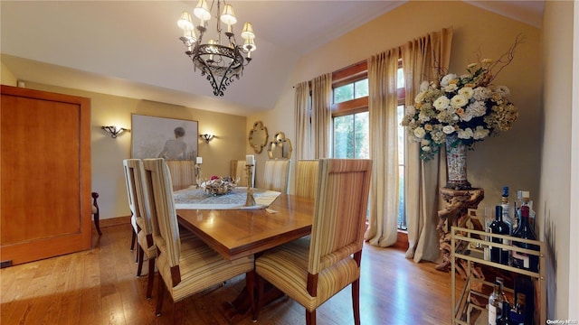 dining area with light wood-type flooring, an inviting chandelier, and lofted ceiling