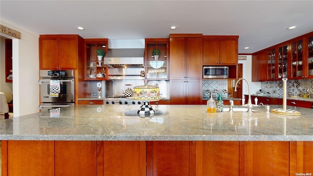 kitchen featuring wall chimney range hood, sink, tasteful backsplash, light stone counters, and stainless steel appliances