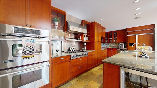 kitchen with light stone countertops, appliances with stainless steel finishes, backsplash, wall chimney exhaust hood, and beverage cooler