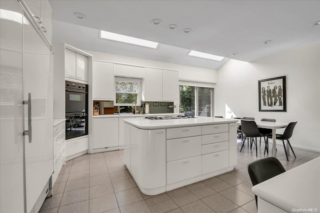 kitchen with white cabinetry, a center island, sink, double oven, and stainless steel gas stovetop