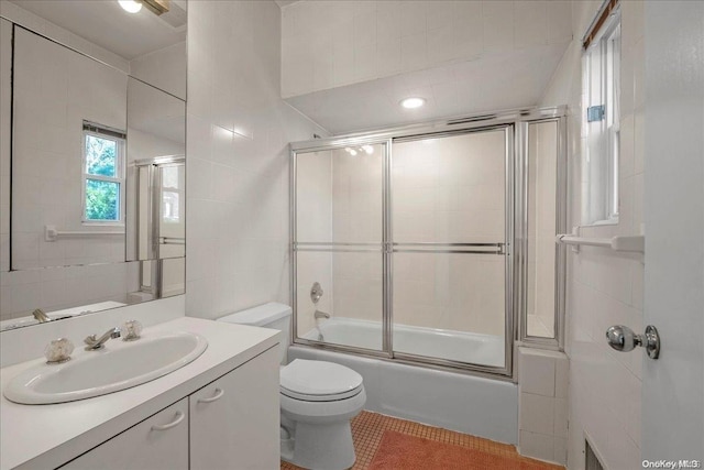 full bathroom featuring vanity, tile patterned floors, bath / shower combo with glass door, toilet, and tile walls