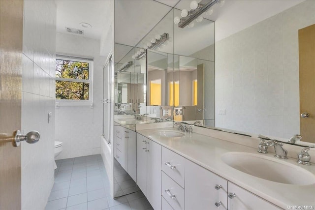 full bathroom with combined bath / shower with glass door, tile patterned floors, toilet, vanity, and tile walls