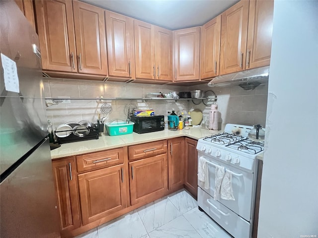 kitchen featuring white range with gas stovetop, backsplash, and stainless steel refrigerator