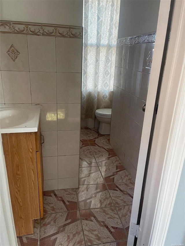 bathroom featuring tile patterned floors, vanity, toilet, and tile walls