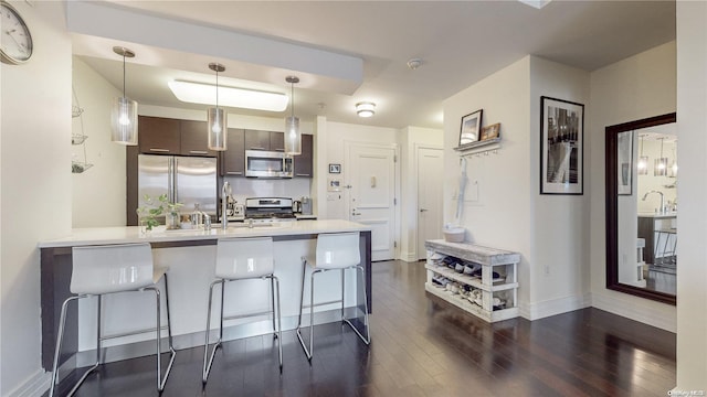 kitchen featuring dark brown cabinetry, dark wood-type flooring, kitchen peninsula, a kitchen bar, and appliances with stainless steel finishes