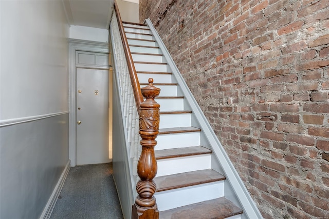 staircase with carpet floors and brick wall