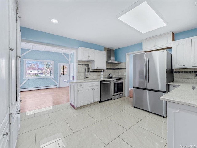 kitchen featuring wall chimney range hood, stainless steel appliances, white cabinetry, and sink