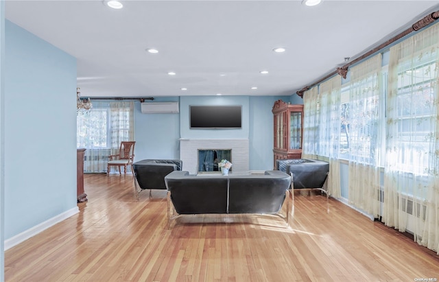 living room with a wall mounted air conditioner, radiator, a brick fireplace, and light hardwood / wood-style flooring