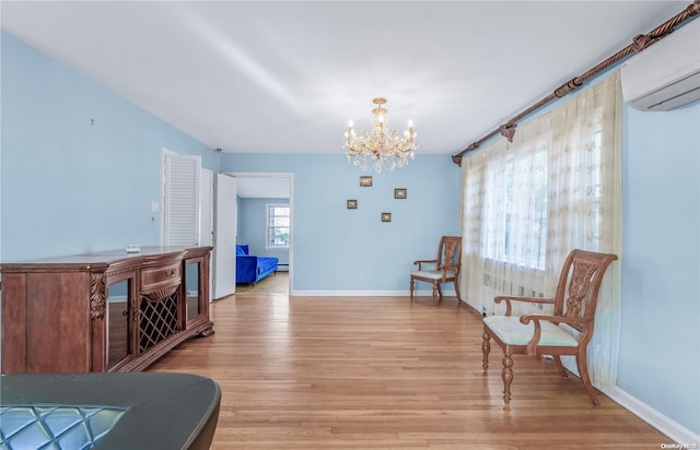 sitting room with light wood-type flooring, an AC wall unit, and a notable chandelier