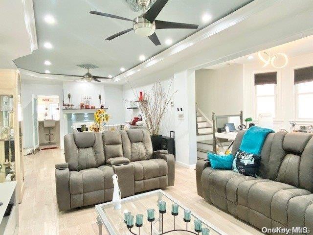 home theater with a tray ceiling, ornamental molding, and light wood-type flooring