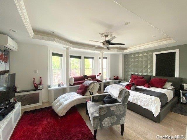 bedroom with ceiling fan, a raised ceiling, a wall unit AC, and light hardwood / wood-style flooring