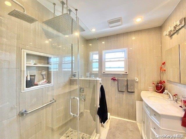 bathroom featuring vanity, a shower with shower door, and tile walls