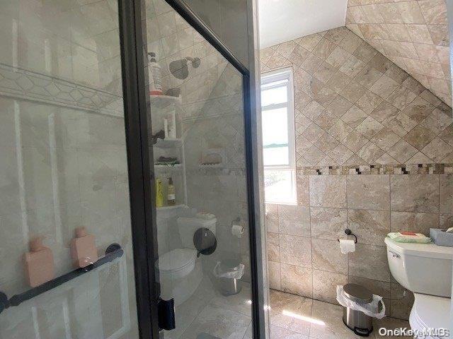 bathroom featuring toilet, walk in shower, lofted ceiling, and tile walls