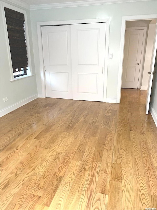 unfurnished bedroom with light wood-type flooring, crown molding, and a closet