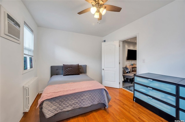 bedroom with ceiling fan, radiator heating unit, a wall mounted AC, light hardwood / wood-style floors, and vaulted ceiling