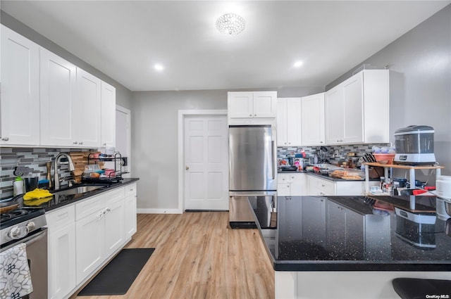 kitchen with white cabinets, appliances with stainless steel finishes, light hardwood / wood-style floors, and decorative backsplash