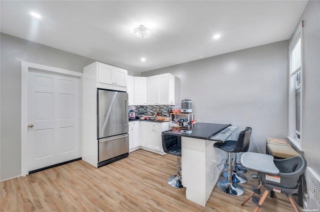 kitchen featuring stainless steel refrigerator, white cabinetry, kitchen peninsula, and light hardwood / wood-style flooring