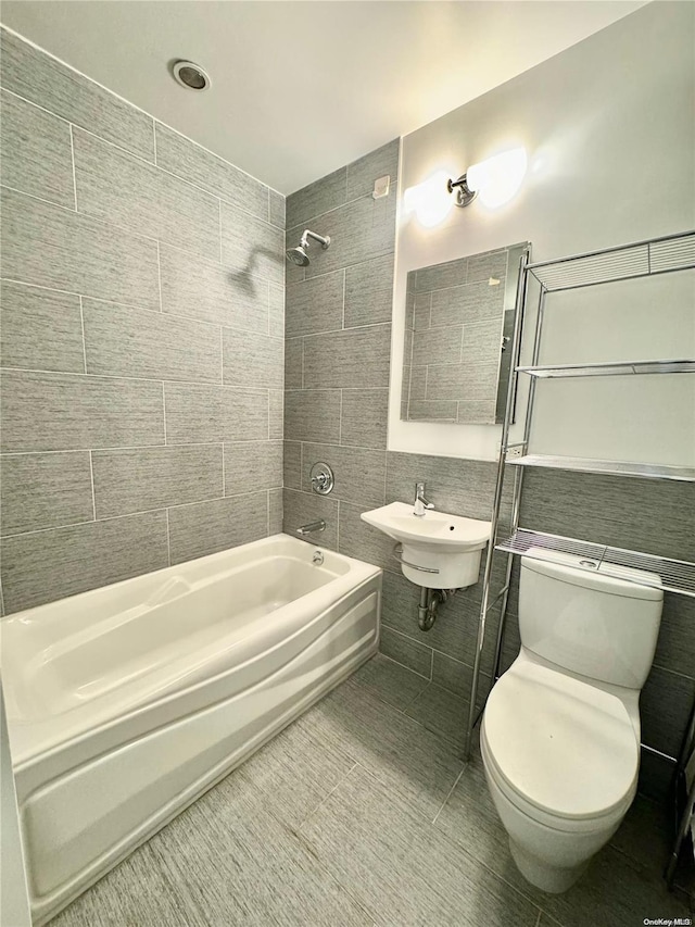 full bathroom featuring tile patterned floors, tiled shower / bath combo, sink, tile walls, and toilet