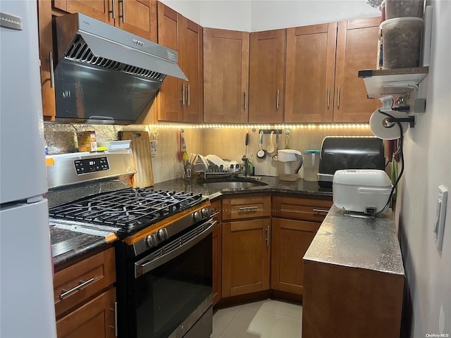 kitchen with tasteful backsplash, gas stove, sink, white refrigerator, and light tile patterned flooring