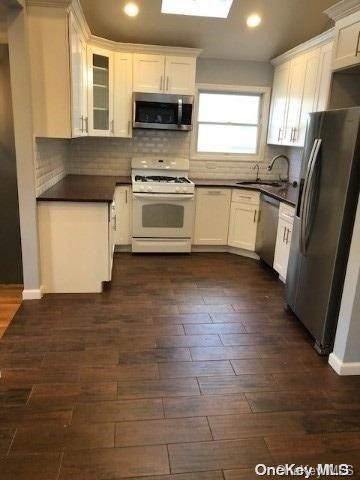 kitchen with white cabinetry, sink, dark wood-type flooring, stainless steel appliances, and tasteful backsplash