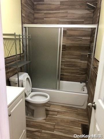 full bathroom with hardwood / wood-style floors, vanity, toilet, and bath / shower combo with glass door