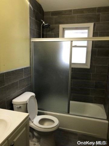 full bathroom with toilet, vanity, tile walls, and combined bath / shower with glass door