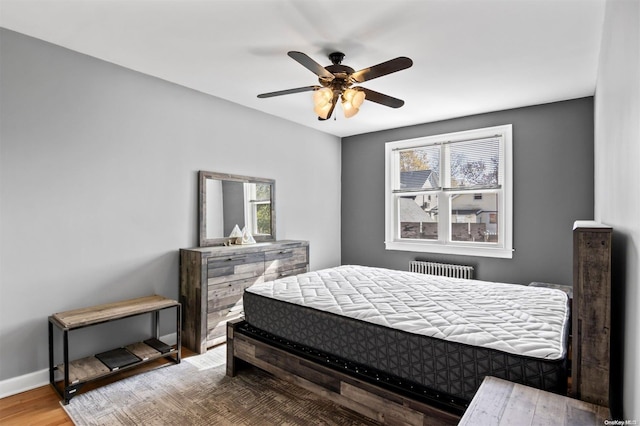 bedroom featuring hardwood / wood-style flooring, ceiling fan, radiator, and multiple windows