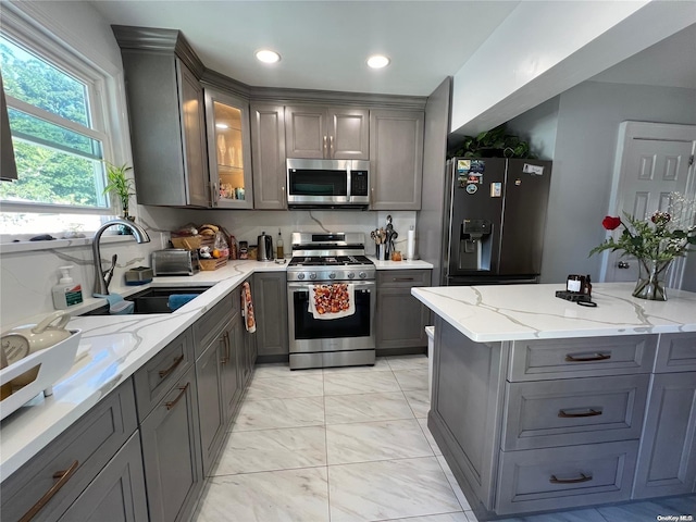 kitchen with gray cabinetry, light stone countertops, sink, and appliances with stainless steel finishes