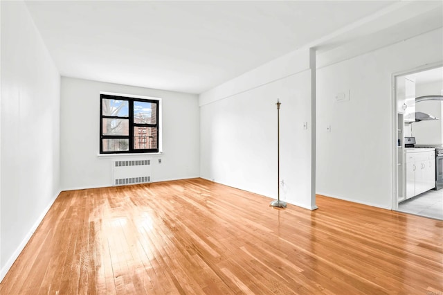 unfurnished room featuring radiator heating unit and light hardwood / wood-style flooring