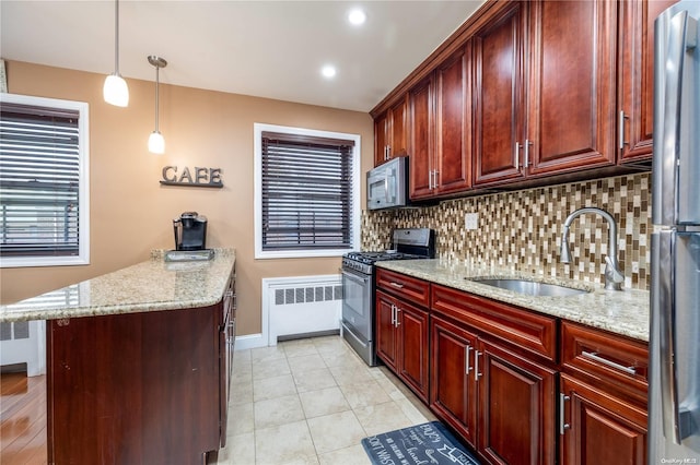 kitchen featuring radiator, sink, stainless steel appliances, light stone counters, and decorative light fixtures