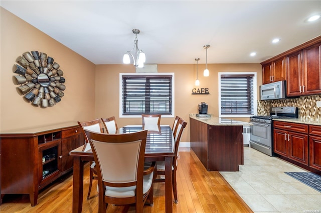 kitchen featuring pendant lighting, an inviting chandelier, light stone countertops, light wood-type flooring, and appliances with stainless steel finishes