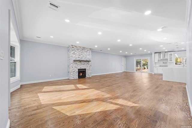 unfurnished living room featuring a stone fireplace, crown molding, and light hardwood / wood-style floors