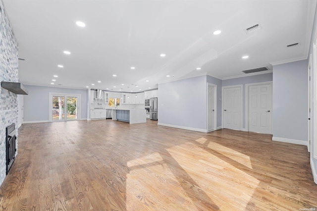 unfurnished living room with light wood-type flooring, a stone fireplace, and ornamental molding