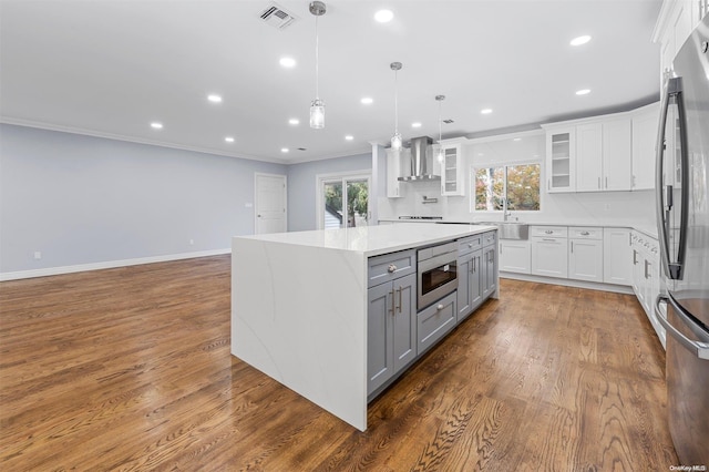 kitchen featuring pendant lighting, white cabinetry, stainless steel appliances, and wall chimney range hood