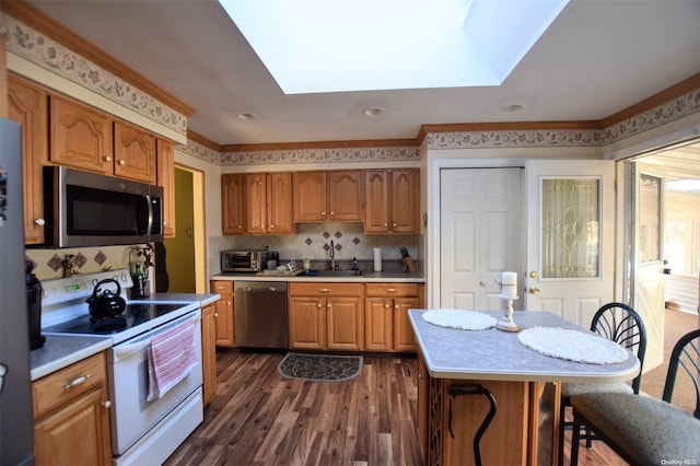 kitchen featuring a skylight, stainless steel appliances, dark hardwood / wood-style floors, crown molding, and a kitchen bar