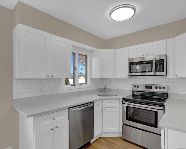 kitchen featuring white cabinets, light wood-type flooring, backsplash, and appliances with stainless steel finishes